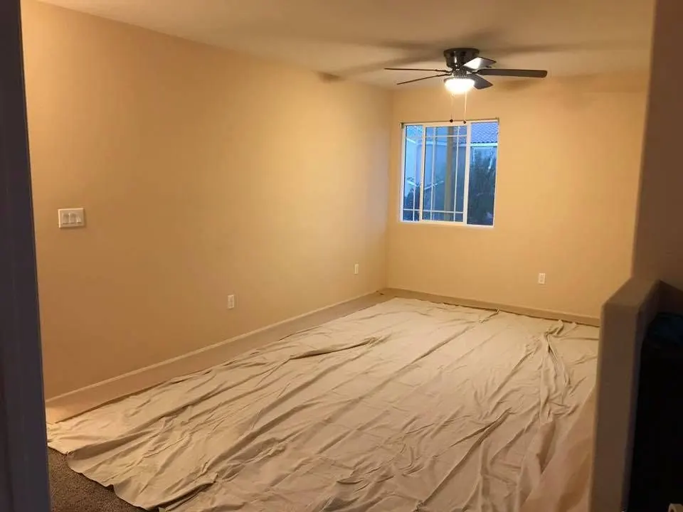 Before: master bedroom with dated tan builder paint in a Las Vegas home, floors protected for repaint