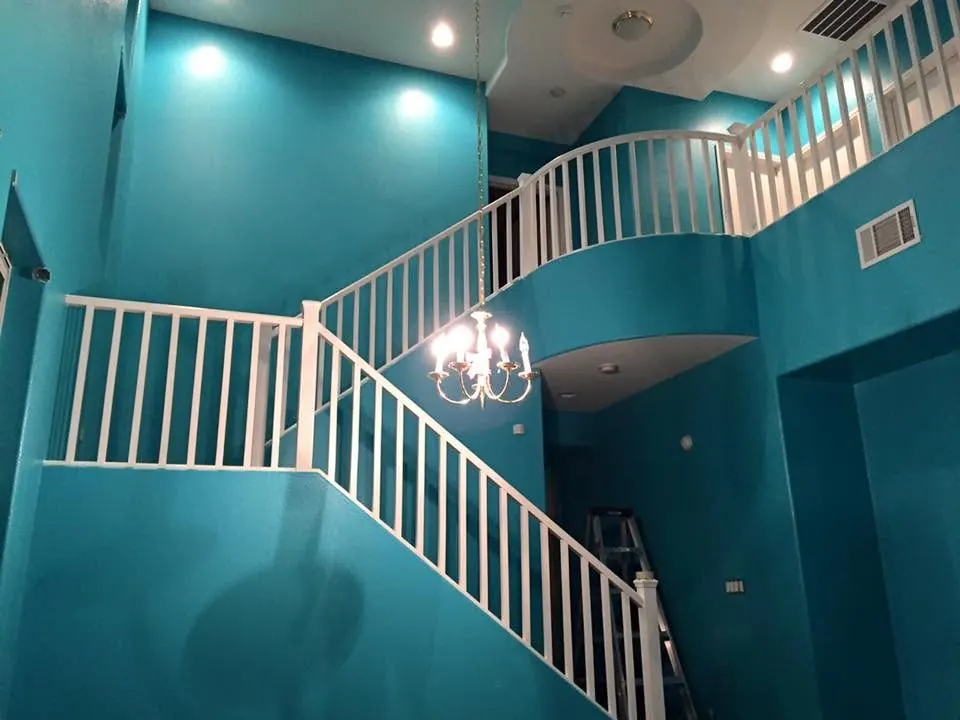 Two-story vaulted stairwell painted a custom teal with crisp white railings by MK Painting Las Vegas